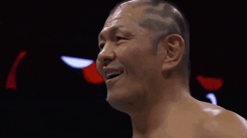 a man without a shirt is laughing with his mouth open in a boxing ring .