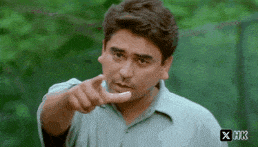 a man in a green shirt is pointing at the camera with the letters hk on the bottom right