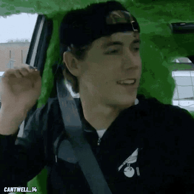a man wearing a black hat and a black jacket is sitting in a green car