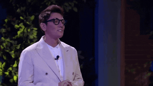 a man in a suit and glasses is standing in front of a microphone and smiling .