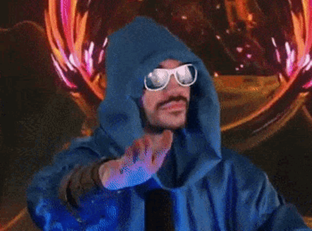 a man wearing sunglasses and a blue hood is waving his hand