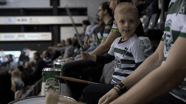 a boy wearing a green and white shirt with the number 7 on it playing drums