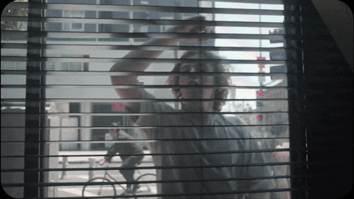 a man is looking out a window with blinds on