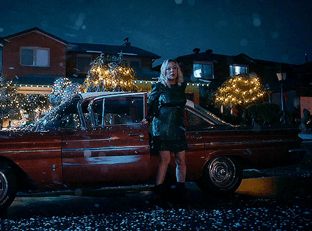 a woman in a green dress stands in front of a car