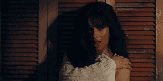 a woman in a white sweater stands in front of shutters