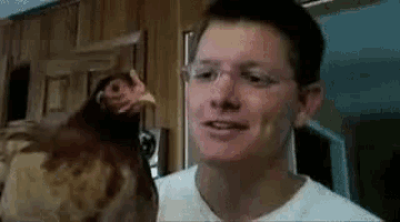 a man with glasses is holding a chicken in his arms .