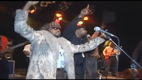 a man in a fur coat sings into a microphone on stage