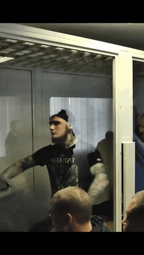 a man in a black shirt that says " aehtat " is standing in a room