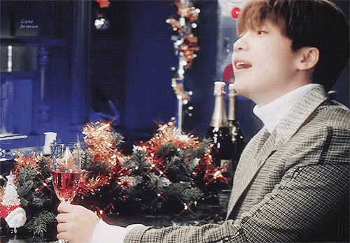 a man holds a glass of champagne in front of a christmas tree