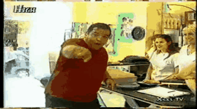 a man in a red shirt is pointing at the camera while standing in front of a counter with a xcat tv logo on it