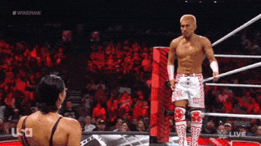 a wrestler is standing in a wrestling ring talking to a woman in front of a crowd ..