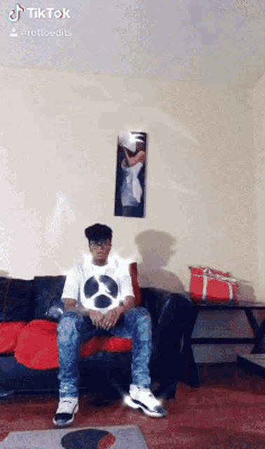 a man is sitting on a couch in a living room with a picture on the wall behind him that says tiktok