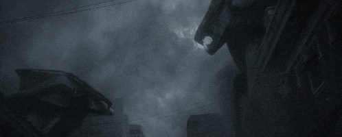 a giant robot is standing on top of a building in the middle of a city at night .