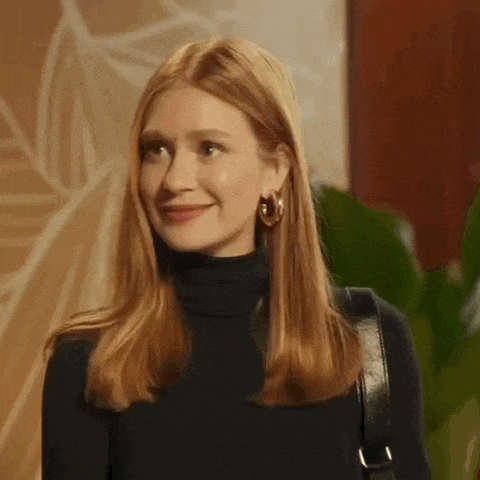 a woman with red hair is wearing a black turtleneck and earrings .
