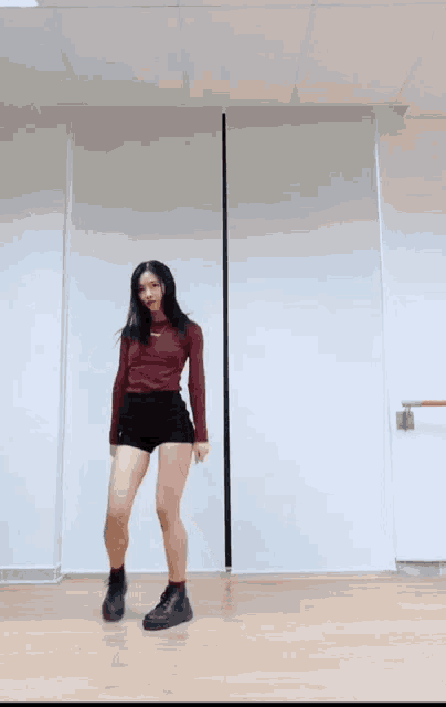 a woman in a red top and black shorts is dancing in a dance studio .