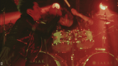 a man playing drums in a dark room with a red light behind him