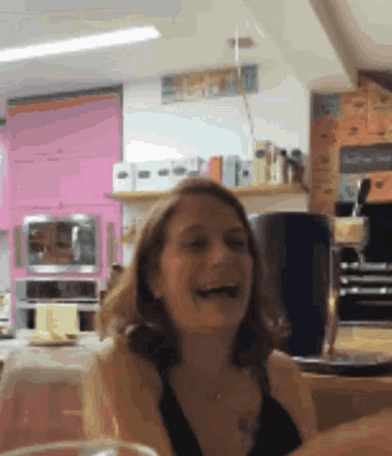 a woman is laughing in a kitchen with a pink oven in the background