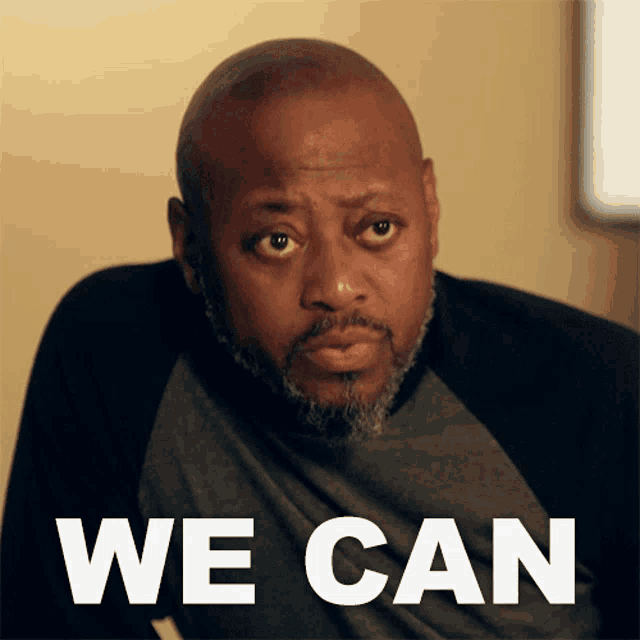a man is sitting in front of a sign that says " we can "
