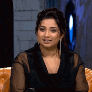 a woman in a black dress and earrings is sitting on a couch and smiling .