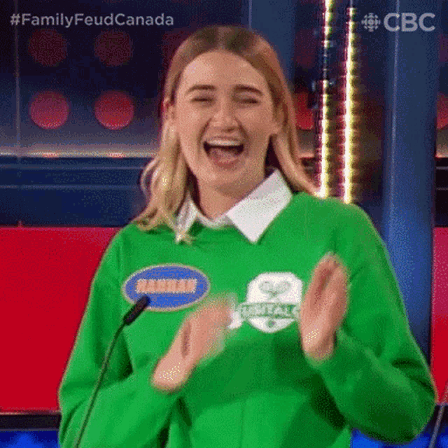 a woman in a green sweater is laughing while clapping her hands .