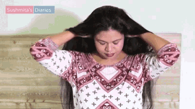 a woman in a pink and white shirt is holding her hair in front of a bed .