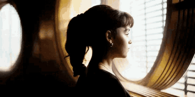 a woman in a ponytail is standing in front of a window .