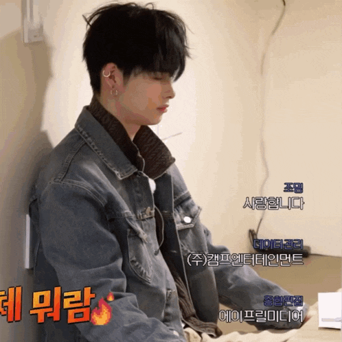 a man wearing a denim jacket is sitting in front of a wall with chinese writing on it