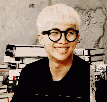 a man wearing glasses and a black shirt smiles in front of a stack of books