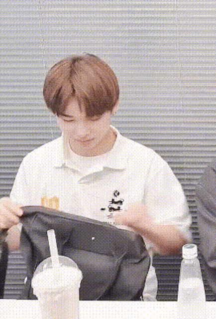 a young man is sitting at a table with a cup of milk and a backpack .