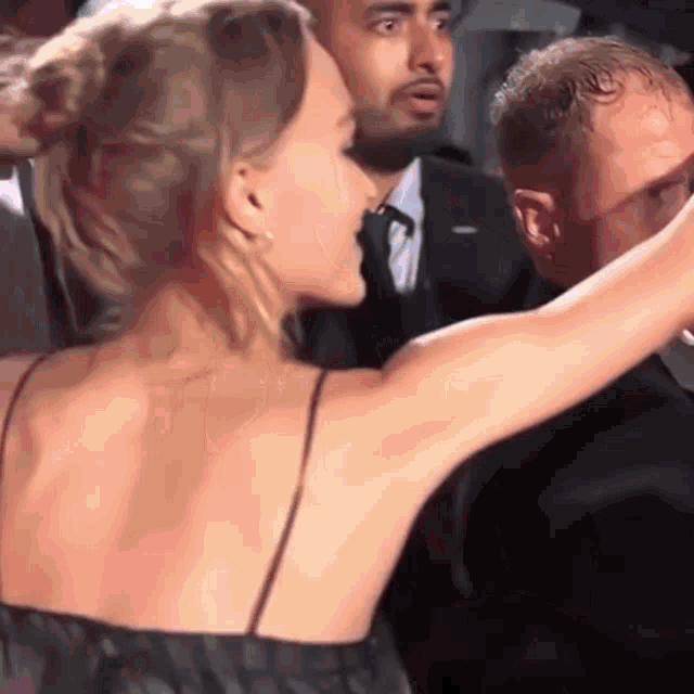 a woman in a black dress is taking a selfie with a man in a suit behind her .