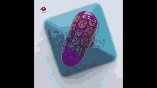 a purple nail with a pattern of cupcakes on it is sitting on a blue block .
