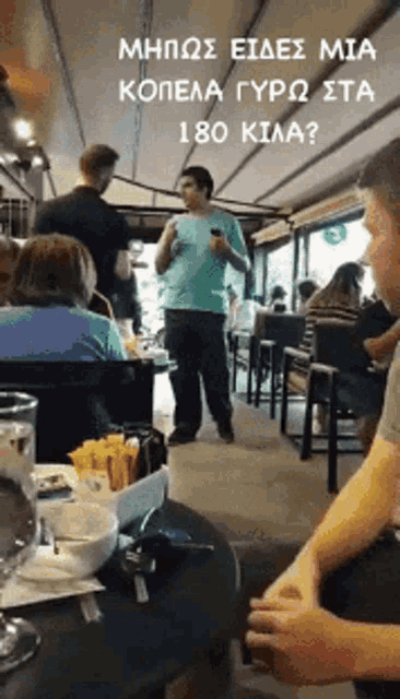 a man in a blue shirt stands in front of a group of people in a restaurant with a sign above him that says 180 kilo