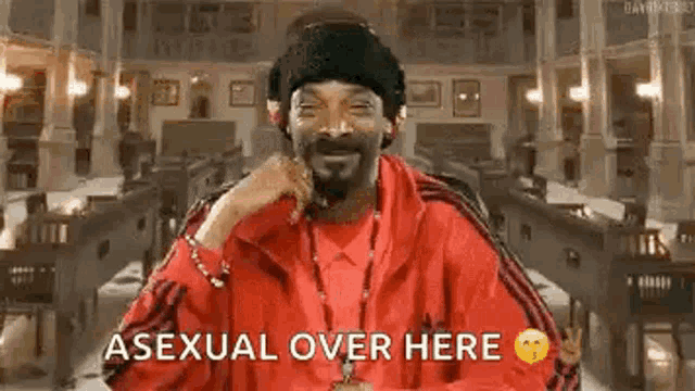 snoop dogg is wearing a red jacket and a black hat and says `` asexual over here '' while smiling .