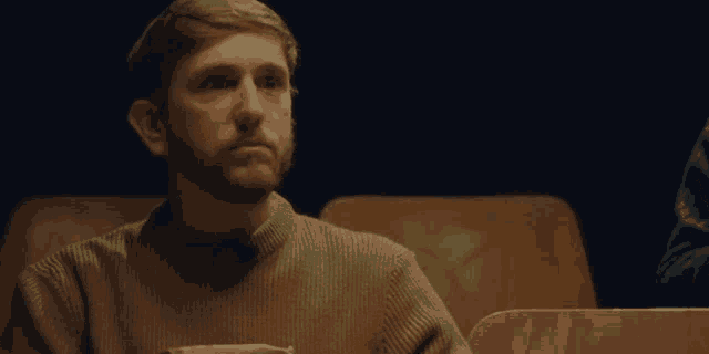 a man with a beard is sitting in a dark room looking at something