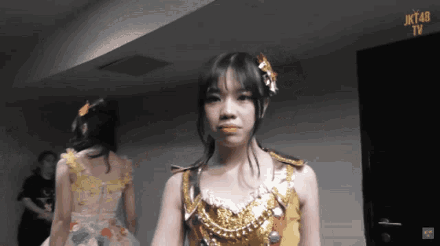 a girl in a gold dress stands in front of a sign that says jk48 tv
