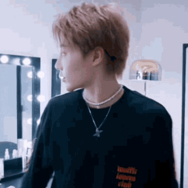 a man wearing a necklace and a black shirt is standing in front of a mirror .