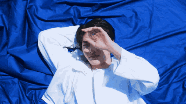 a man in a white shirt laying on a blue sheet