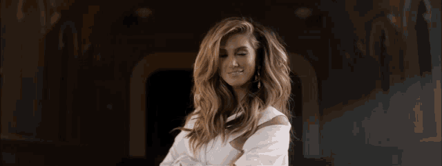 a woman in a white dress with her arms crossed smiles