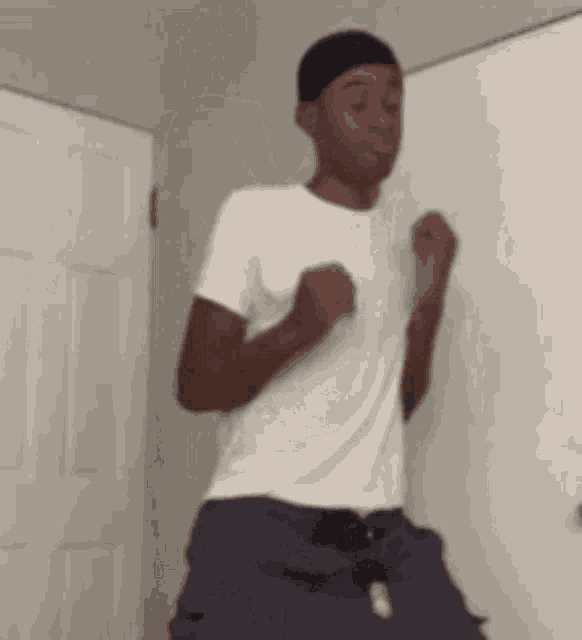 a man in a white shirt and black hat is dancing in front of a white door .