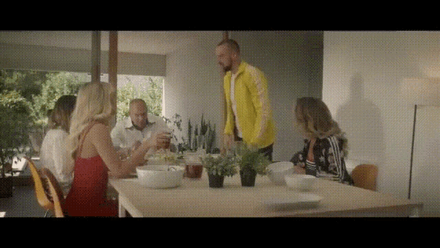 a man in a yellow jacket is standing in front of a table with people sitting at it .