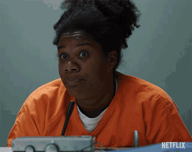 a woman in an orange uniform is sitting at a table with a netflix logo on the bottom