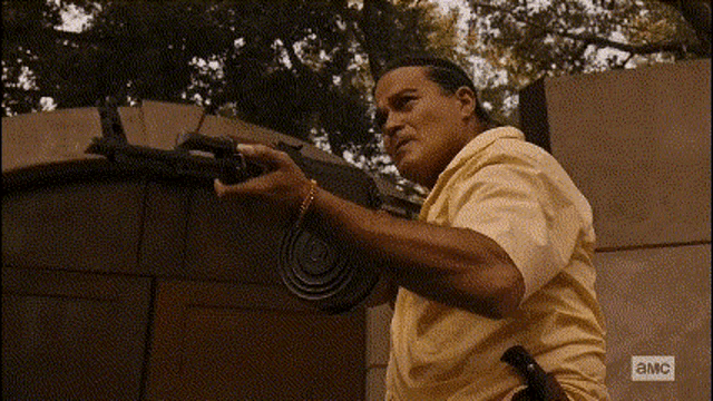 a man in a yellow shirt is holding a gun in front of a wall .