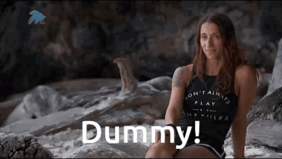 a woman in a black tank top is sitting on a rock on the beach and says dummy !