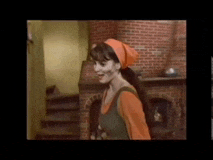 a woman in an orange head scarf is standing in front of a brick fireplace .