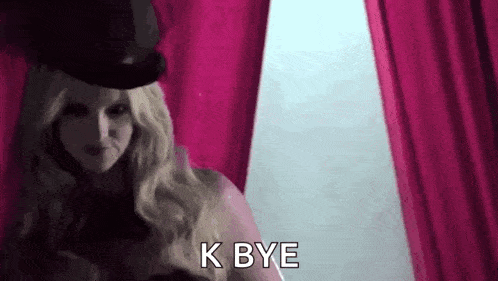a woman wearing a top hat is standing in front of a pink curtain and saying `` k bye '' .