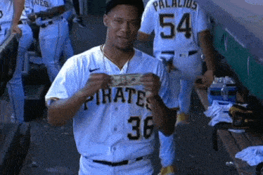 a man in a pirates jersey holds a dollar bill in his hand