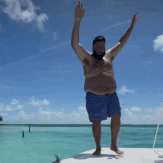 a shirtless man in blue shorts is standing on a boat in the ocean