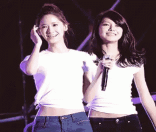 two young women are standing next to each other on a stage holding microphones .