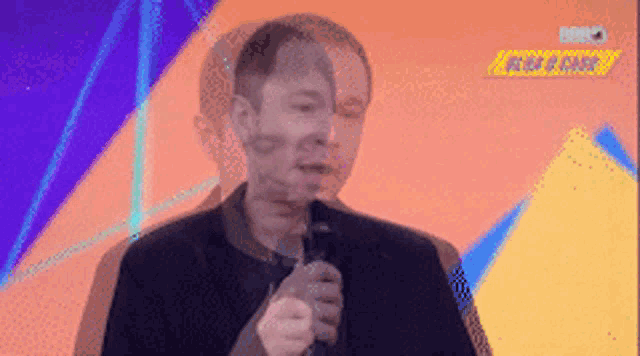 a man in a suit is holding a microphone in front of a purple and orange background .