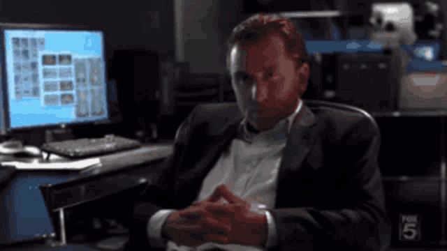 a man in a suit sits in front of a computer with the number 5 on the bottom